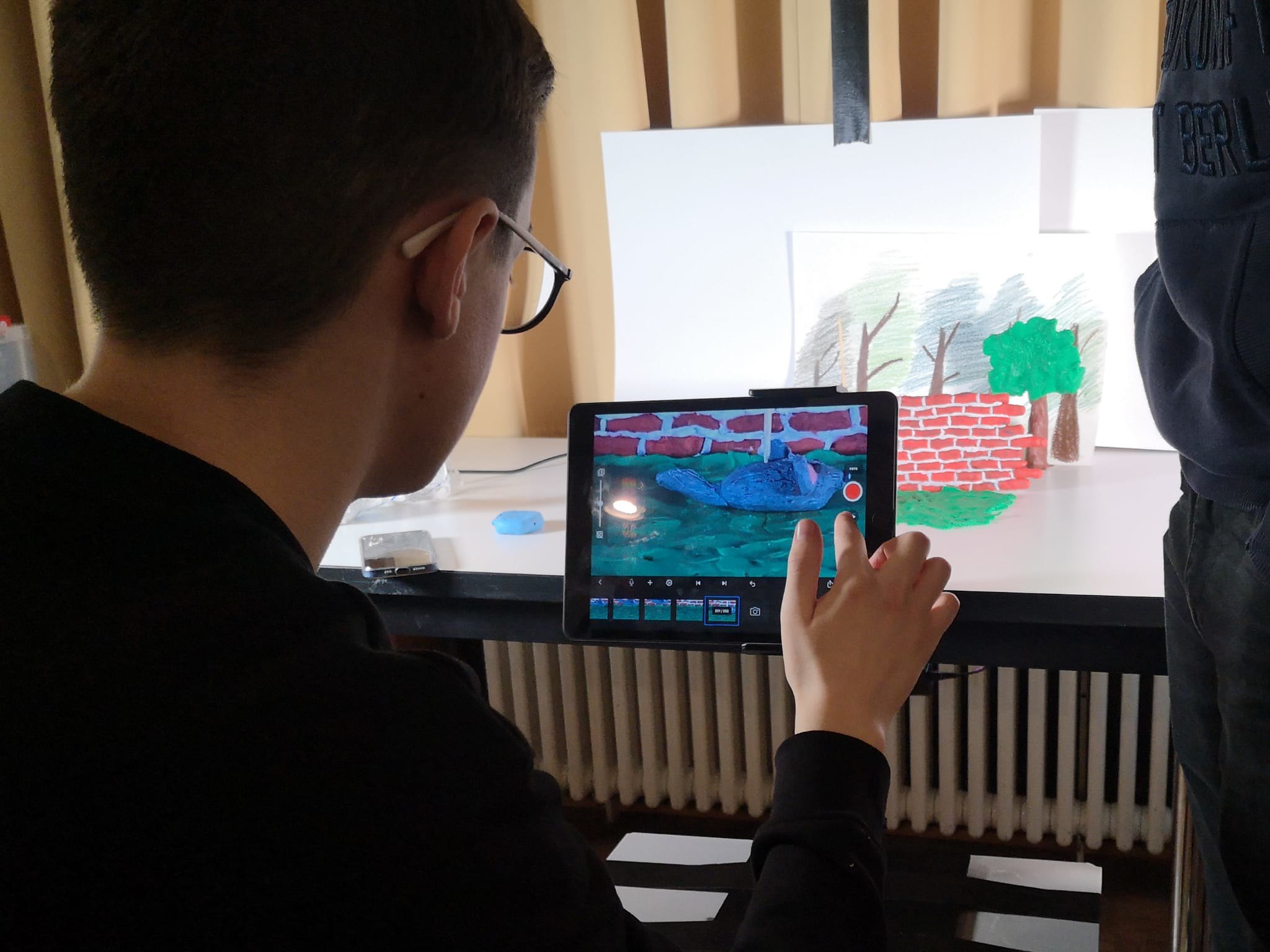Jugendlicher bedient Tablet vor Stop-Motion-Animation mit gezeichnetem Hintergrund und Modell eines blauen Vogels