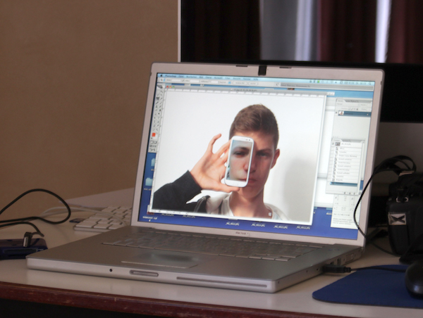 Laptop zeigt Bildbearbeitung mit einem Jugendlichen, der seine Handy mit einem Bild von seinem Ohr in seinem Gesicht genau vor sein Ohr hält