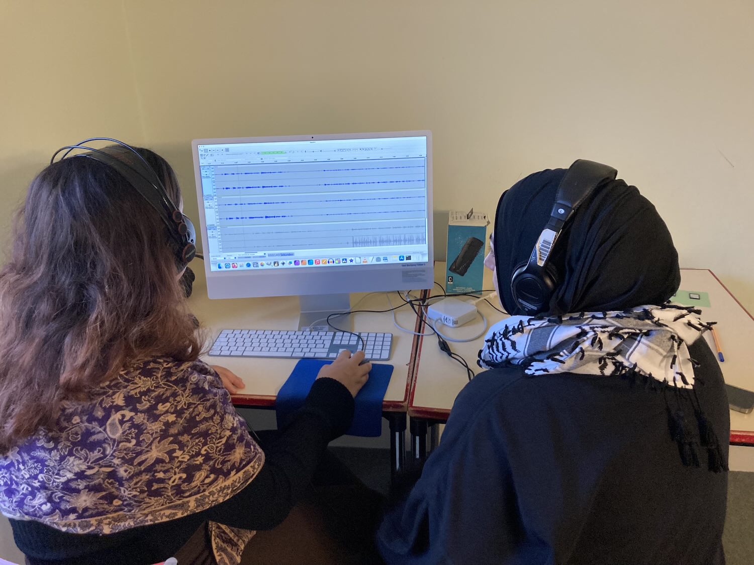 Zwei junge Frauen mit Kopfhörern bearbeiten eine Audiospur auf einem Computerbildschirm, Podcast-Aufnahme im Büro