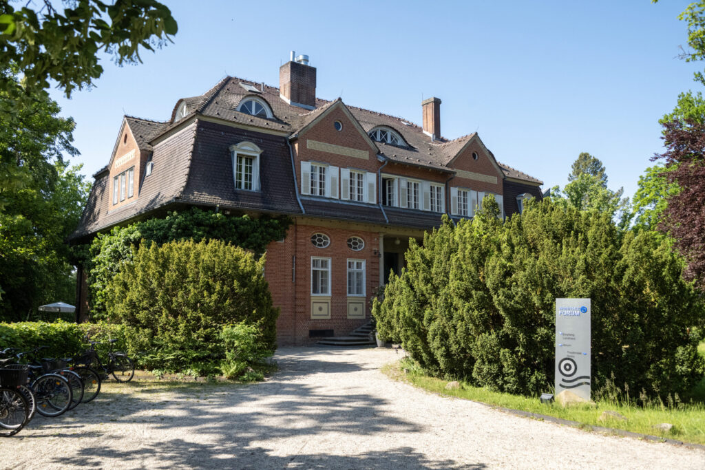 Großes zweistöckiges Backsteingebäude Landhaus mit Mansarddach, umgeben von grünen Büschen und Bäumen, bei klarem Himmel