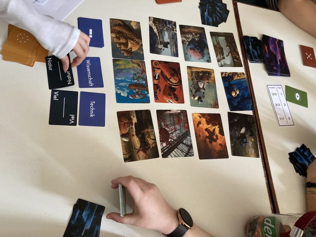 Mehrere Personen spielen ein Kartenspiel mit Karten zu Wissenschaft, Technik und Natur auf einem weißen Tisch.