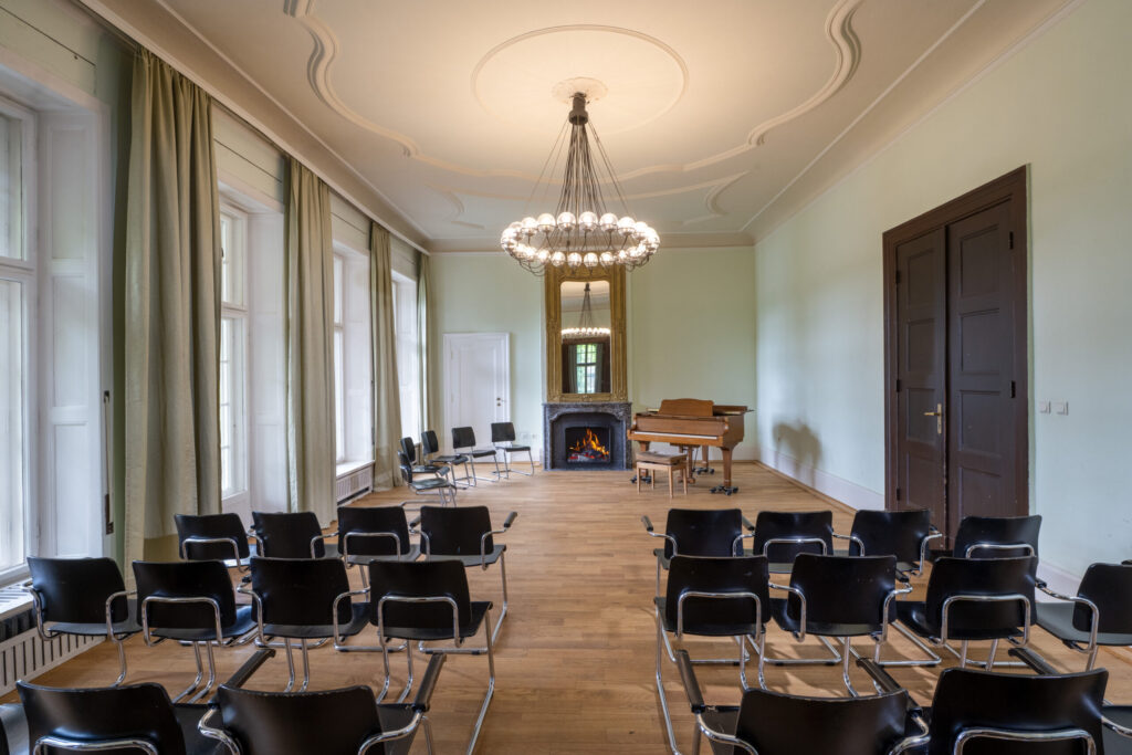 Seminarraum Kaminzimmer mit Reihen schwarzer Stühle, einem Flügel und einem Kamin am Ende des Raums.