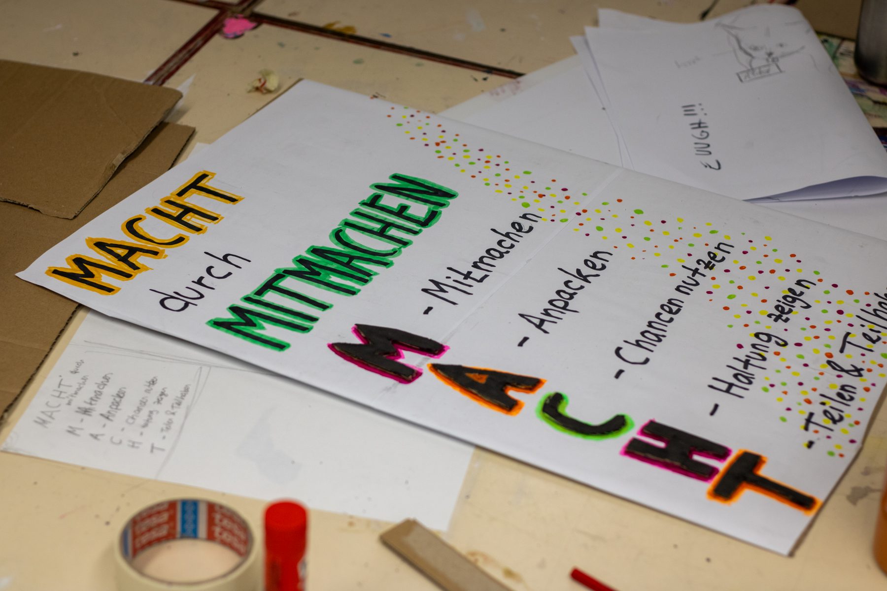 Handgeschriebener Plakattext 'MACHT durch MITMACHEN' mit den Buchstaben M, A, C, H, T erklärt als Mitmachen, Anpacken, Chancen nutzen, Haltung zeigen, Teilen, Teilhaben
