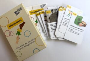 Kartenspiel mit mehreren Karten und einer Schachtel mit der Aufschrift 'Schulheld:in'