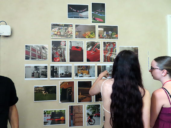 Zwei Personen betrachten eine Wand mit mehreren Fotos, die an einer Wand hängen